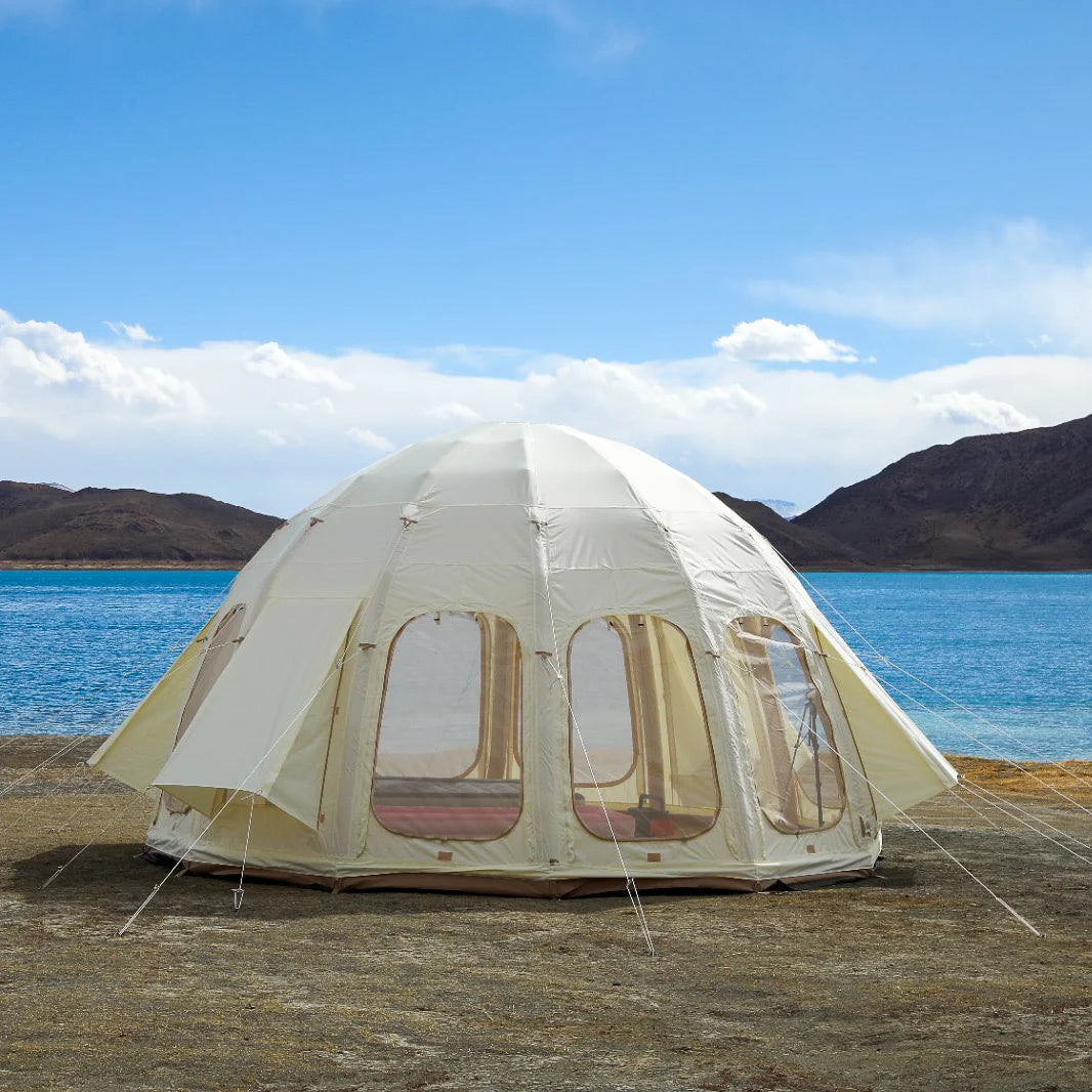 White dome tent with mesh windows on a sandy beach with blue water and mountains in the background