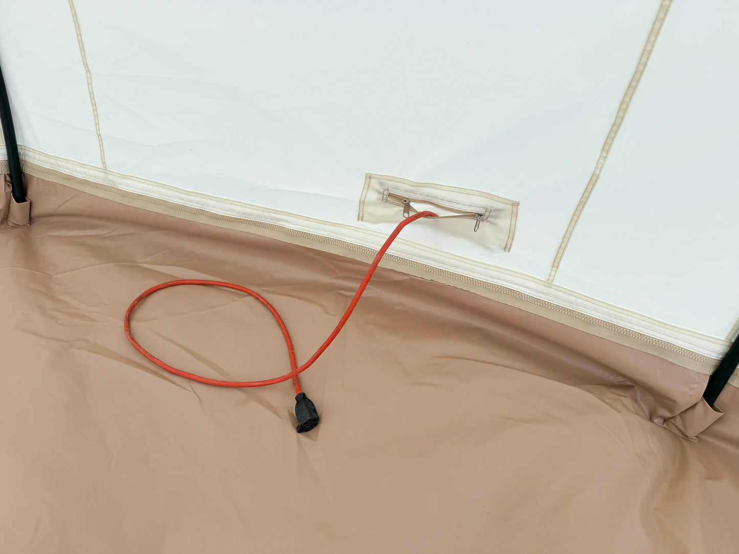 Red extension cord plugged into a power outlet on a beige surface.