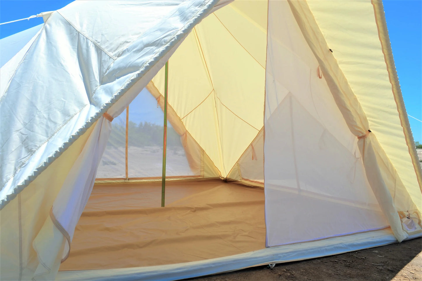 Partial view of a tent with a wooden floor and white walls against a blue sky.