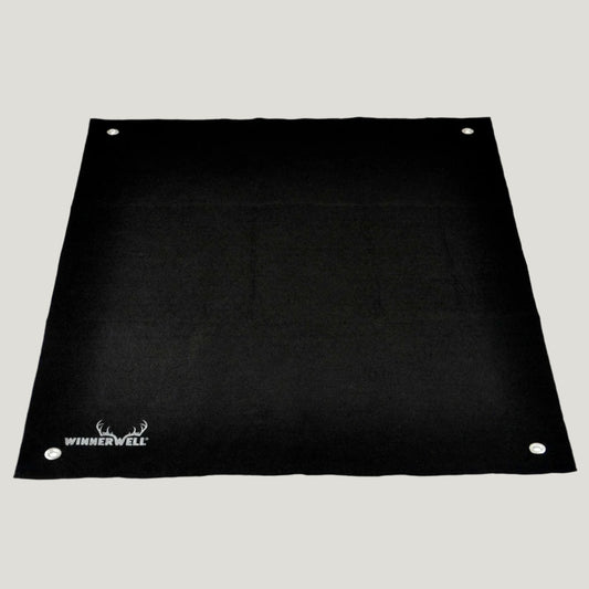 A black, rectangular Winnerwell mat made of fireproof carbon fiber and aluminum foil, designed for use with wood-burning stoves to protect tent floors.