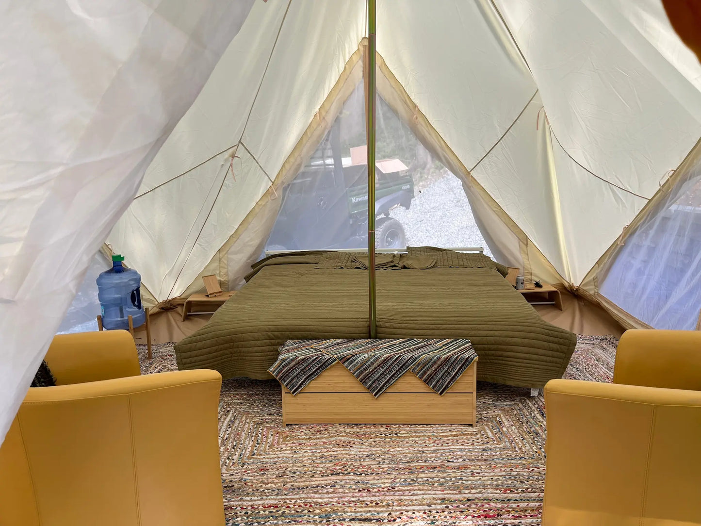 Interior of a tent with a bed and chairs, featuring a scenic view outside.
