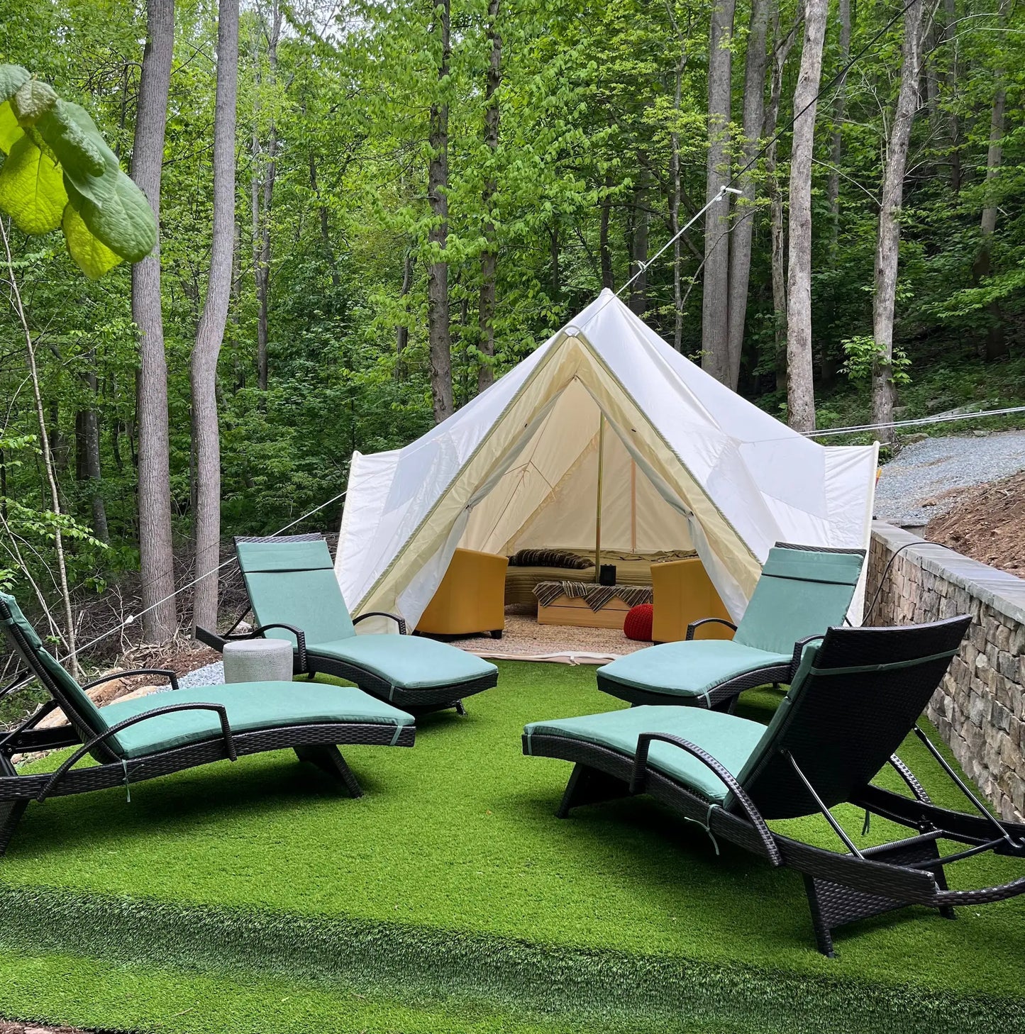 Bell tent in a forest setting with lounge chairs and outdoor furniture.
