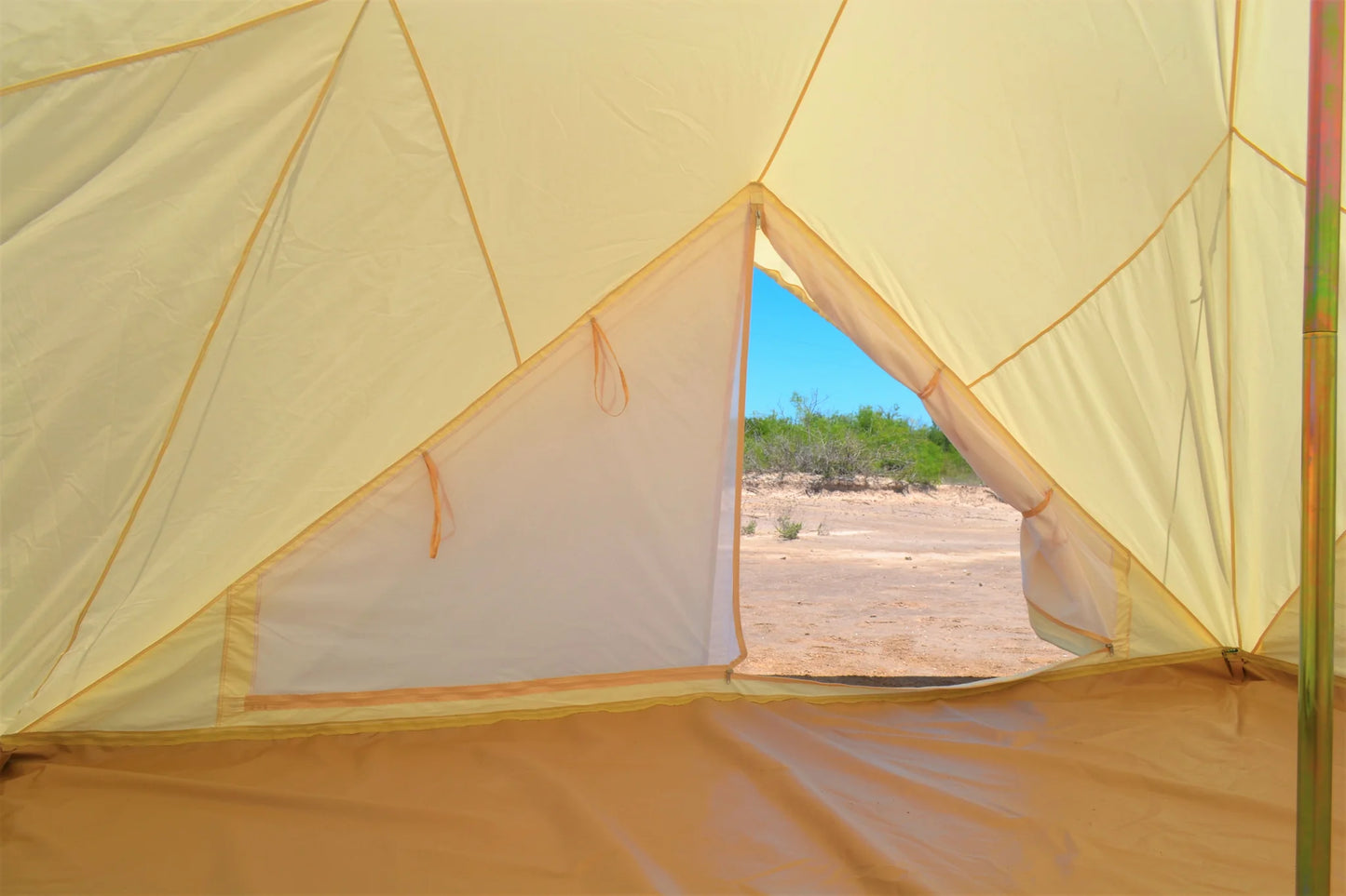 View from inside a yellow tent looking out onto a desert landscape with blue sky.