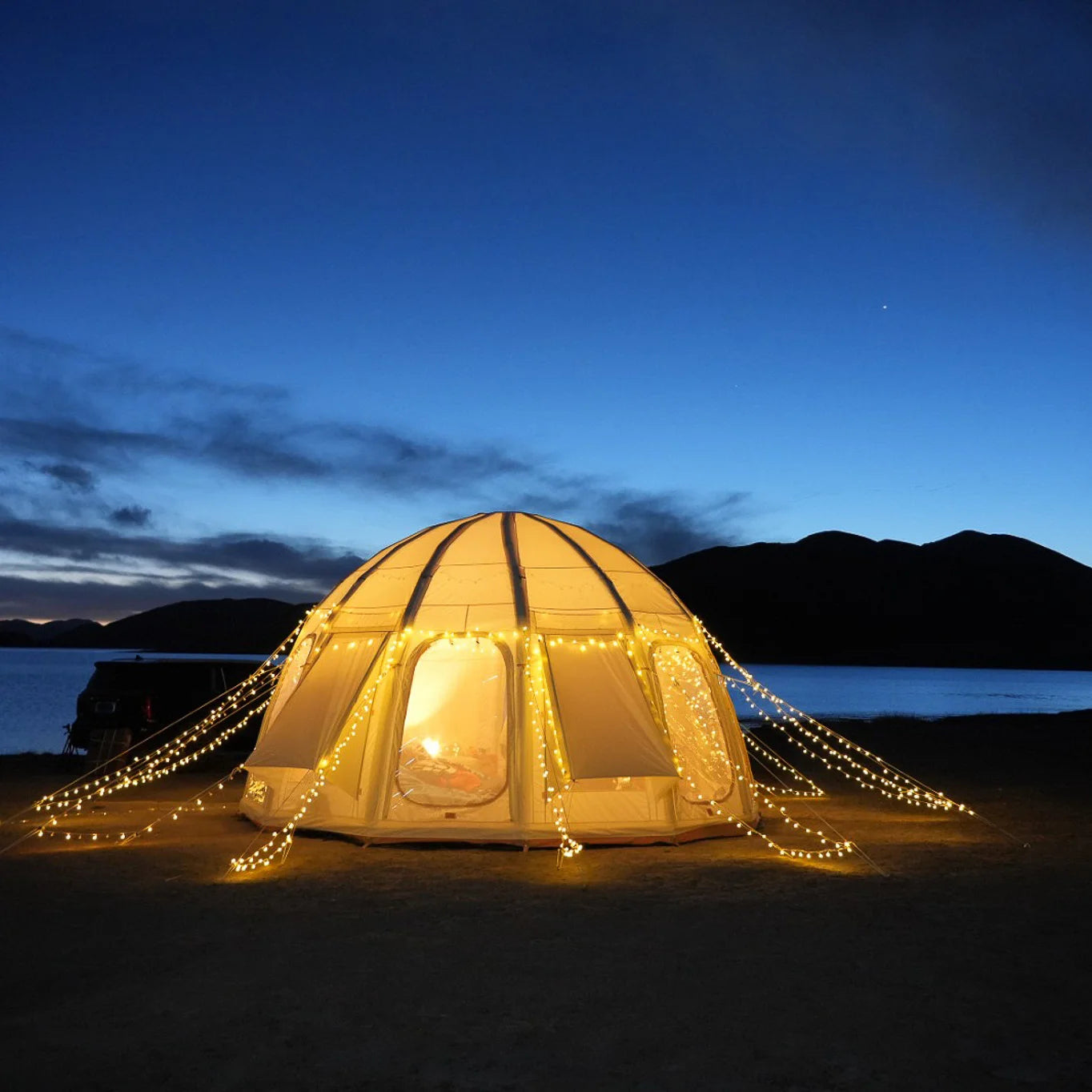 Geodesic dome tent with string lights at night by a body of water