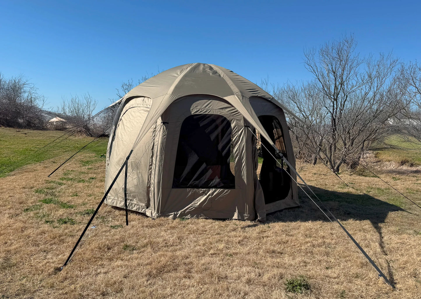 Beige camping tent set up in a grassy field with a clear blue sky.