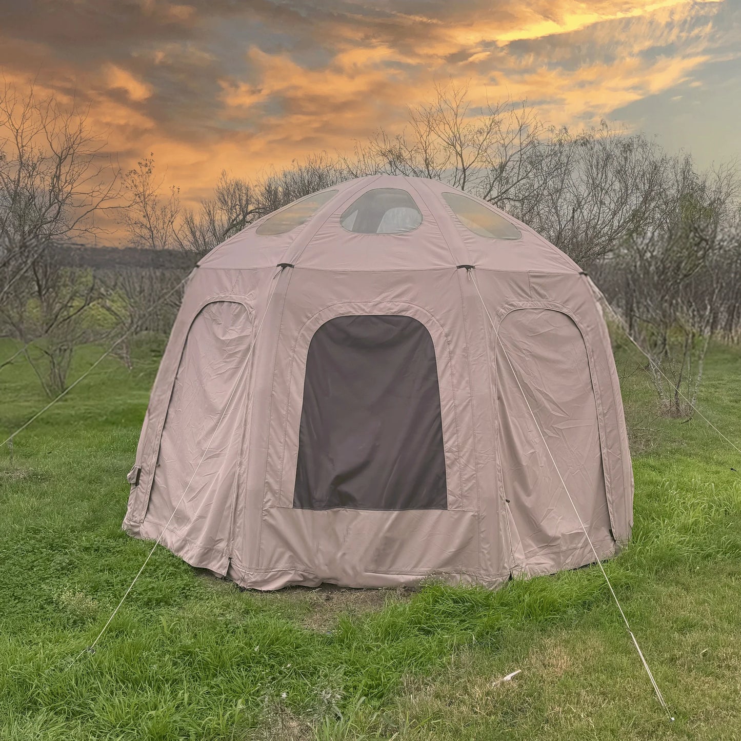 Brown dome-shaped tent in a grassy field with a sunset sky