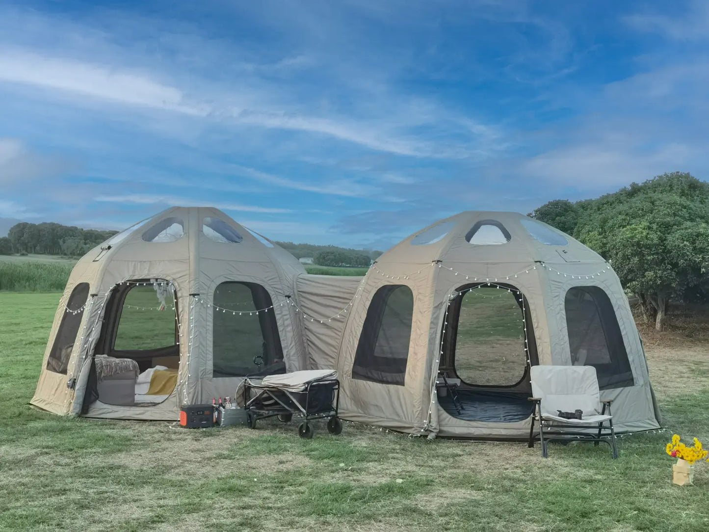 Two beige camping pods with interior views on a grassy field under a blue sky.