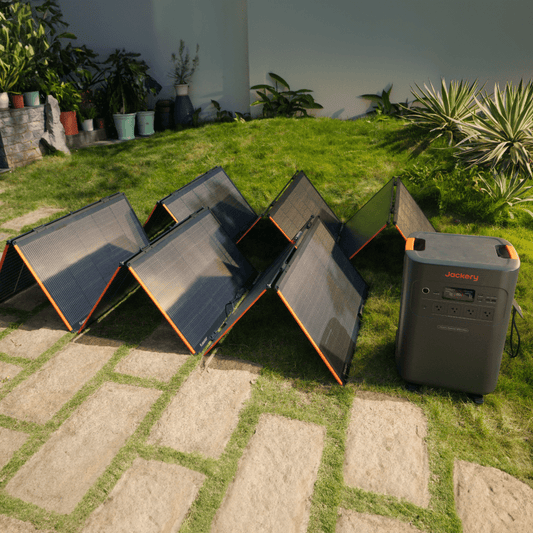 Set of solar panels and a power station on a grassy outdoor area with plants in the background.