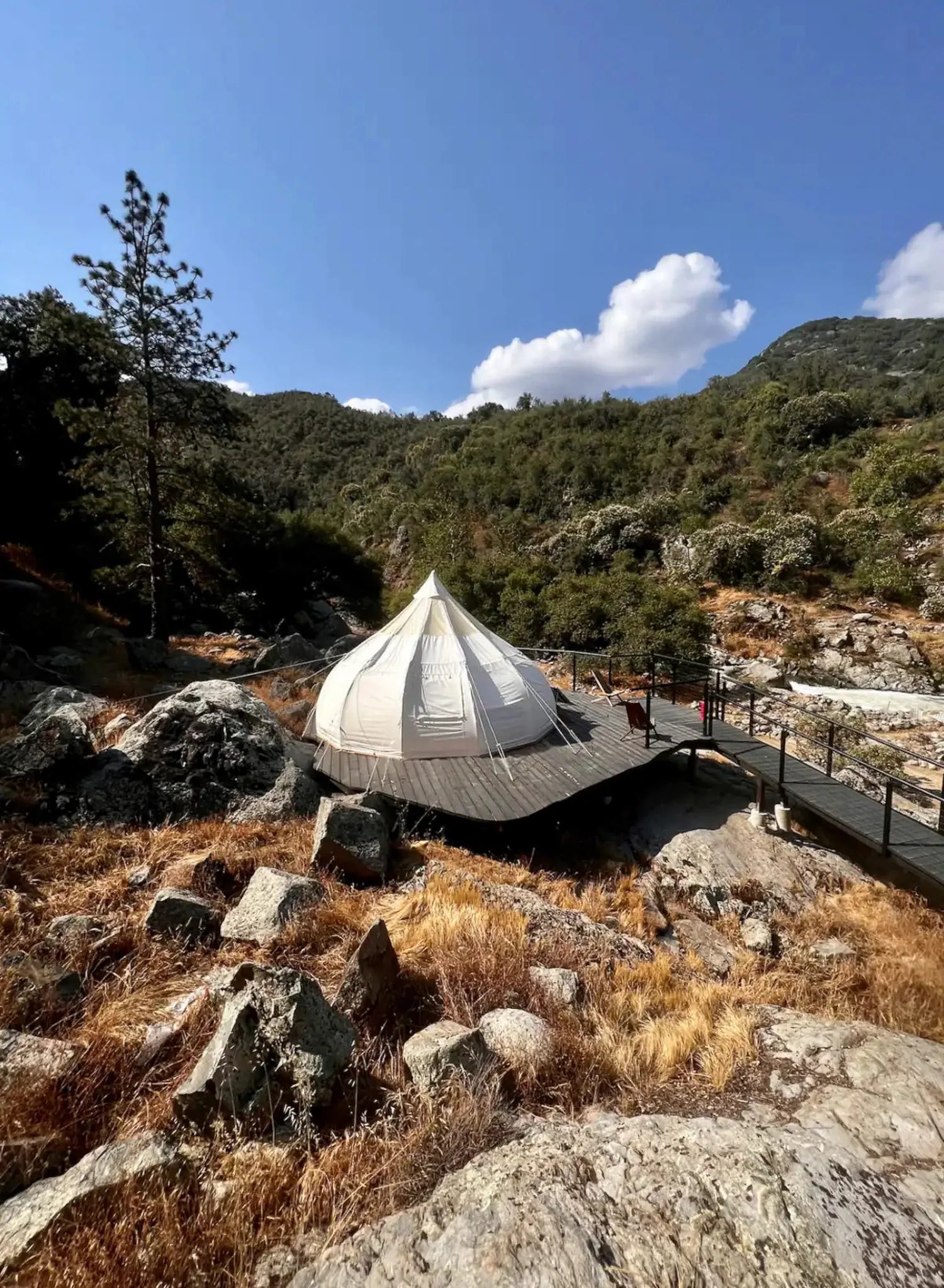 Tented structure in a mountainous landscape with rocky terrain and trees.