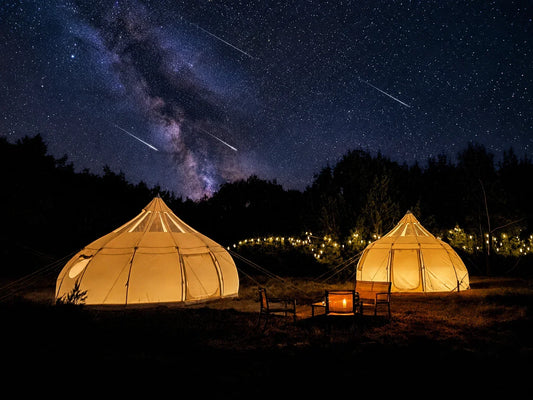 Meteor streaks across a dark night sky above a glowing glamping tent with the Milky Way visible