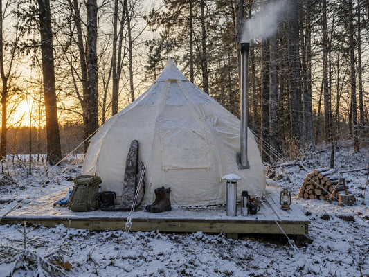 A canvas hunting camp tent in cold weather with frost on the ground and smoke rising from the stove pipe