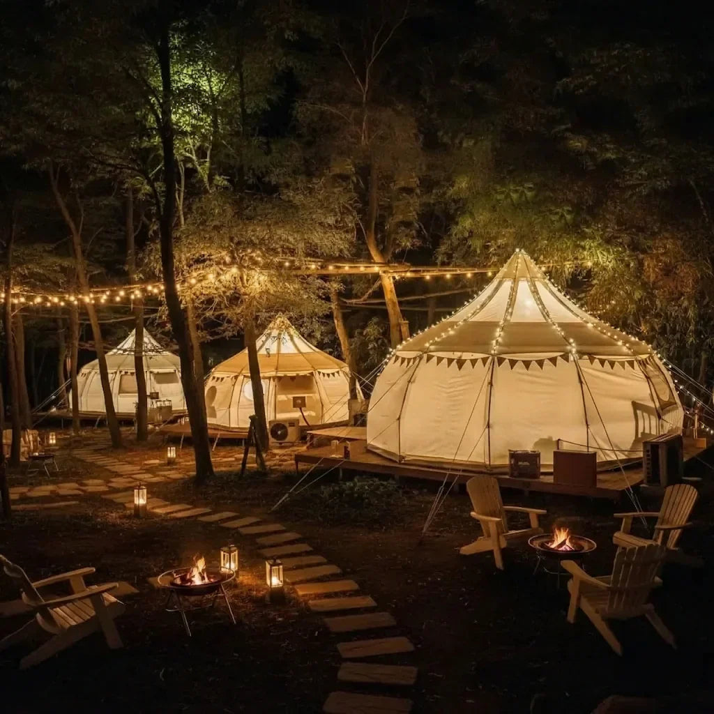 Multiple glamping tents set up on a wooded property at dusk with warm interior lighting and string lights