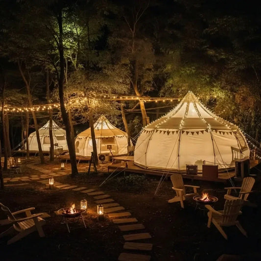 Multiple glamping tents set up on a wooded property at dusk with warm interior lighting and string lights