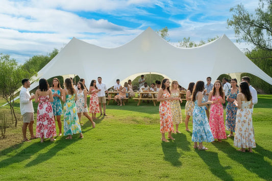 Group of people in colorful dresses standing in a grassy area with a large white tent in the background.