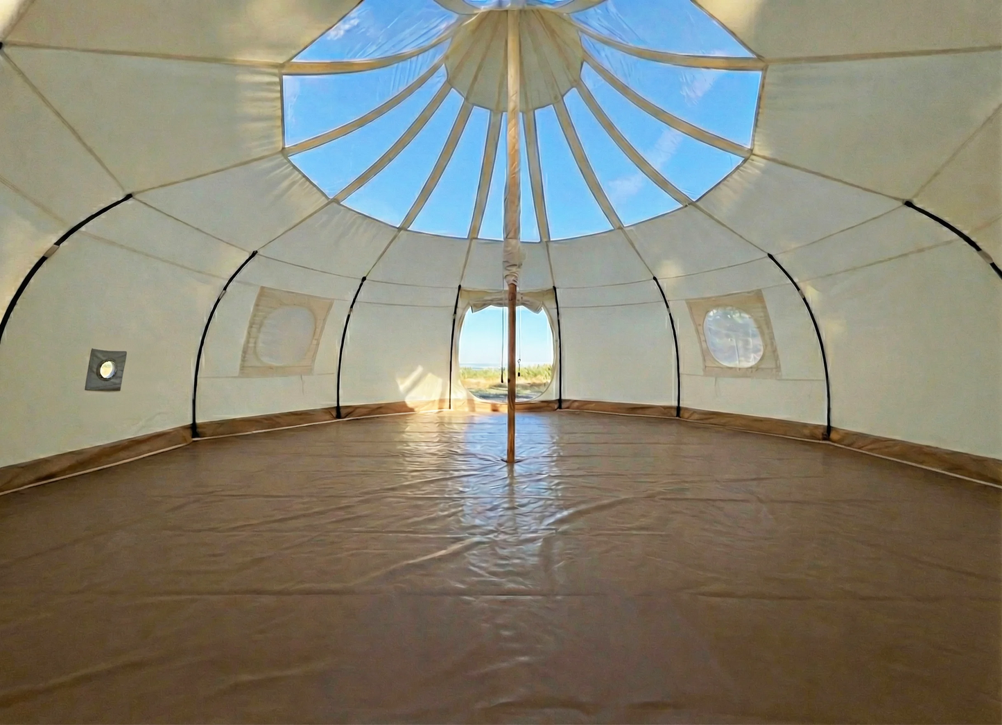 Interior of Astral glamping tent showing transparent skylight ceiling, center pole, stove jack port, round windows, and PVC groundsheet