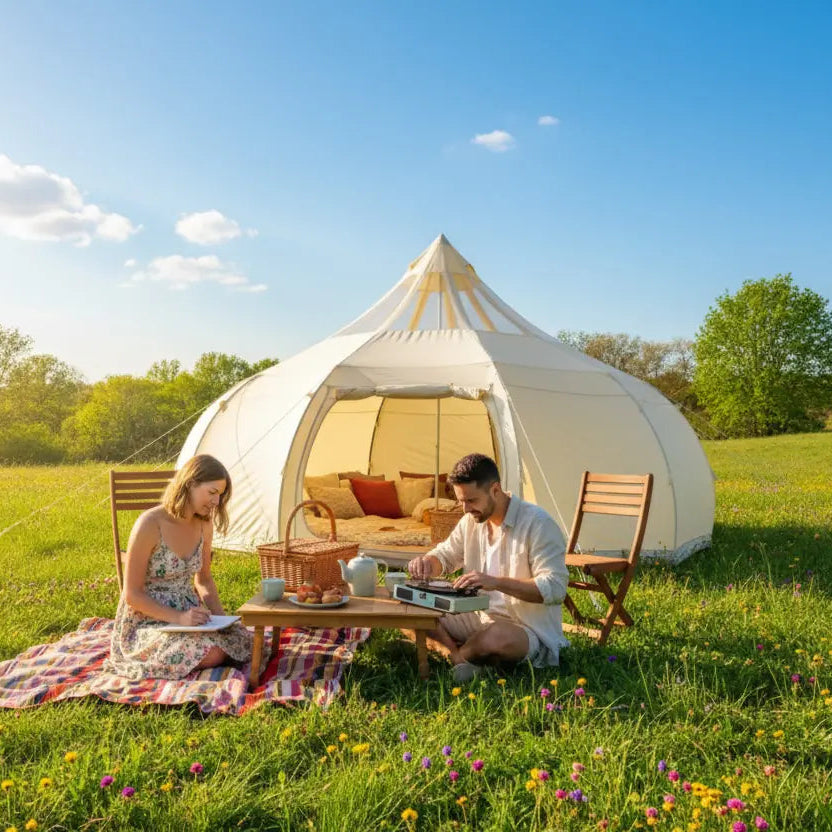Two people sitting at a table outside a white tent in a grassy field with a blue sky.