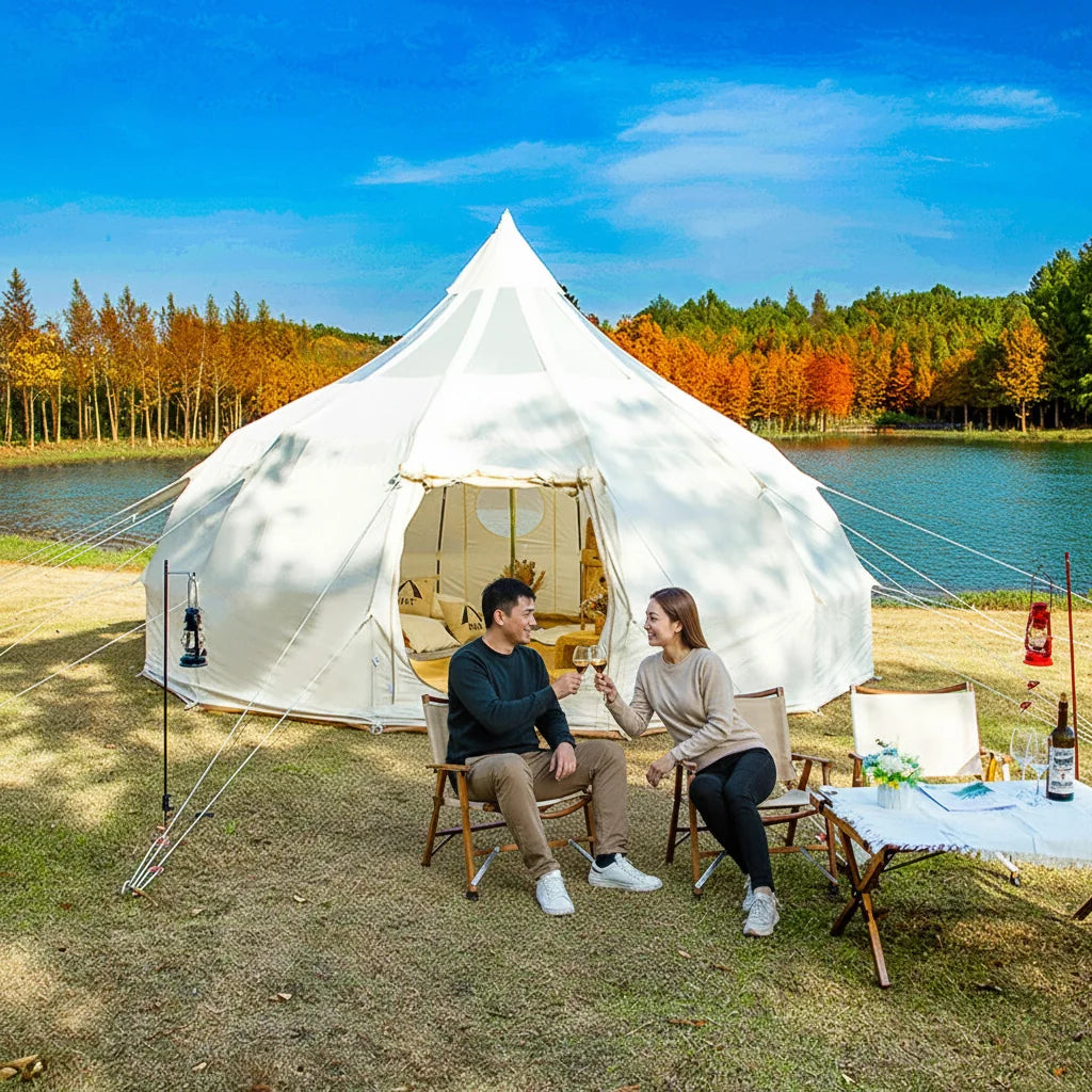 Two people sitting in front of a white tent by a lake with trees in the background