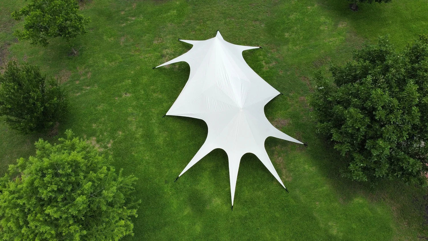 White star-shaped tent on a grassy field with trees around