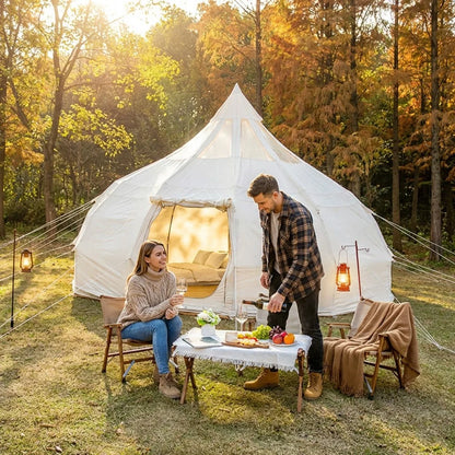 Two people sitting outside a white tent in a forest during sunset.