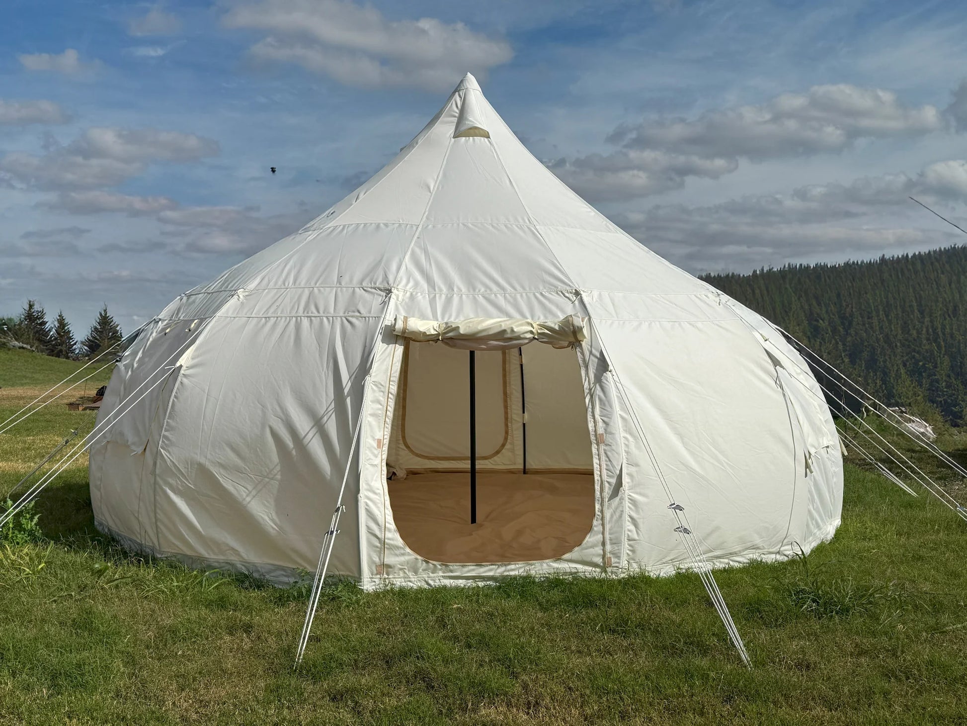 White bell tent in a grassy field with a blue sky and clouds