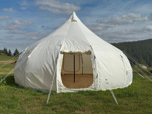 White bell tent in a grassy field with a blue sky and clouds