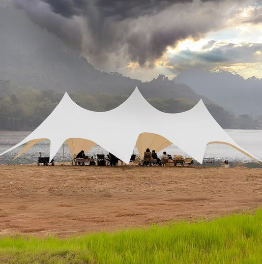 Large white Canopy set up on a beach with people sitting under them, against a backdrop of mountains and clouds.
