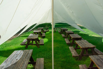 Wooden picnic tables arranged on a grassy area under large white tents.