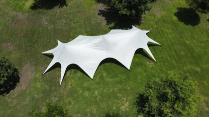 White star-shaped tent on a grassy field with trees