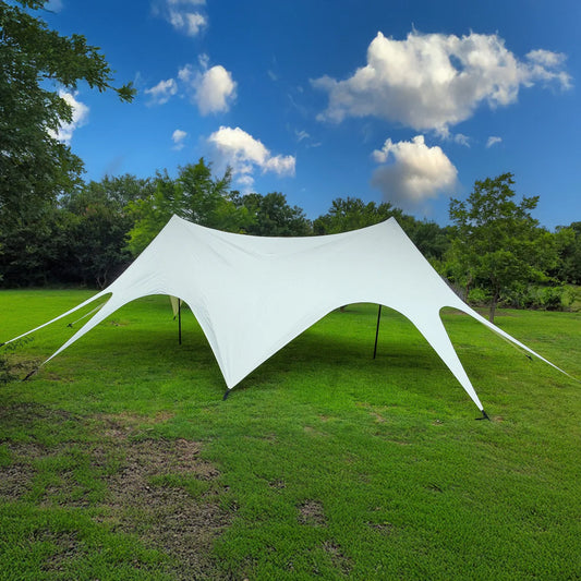 White star-shaped tent set up on a grassy field with trees and blue sky in the background